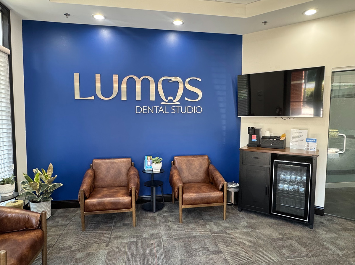 Lumos Dental Studio waiting room with a blue logo wall and brown chairs